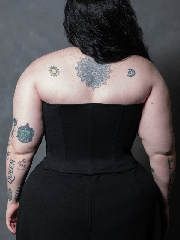 A female model draped in the velvety shadows of gothic glamour, wearing a beautifully tailored black sateen corset.