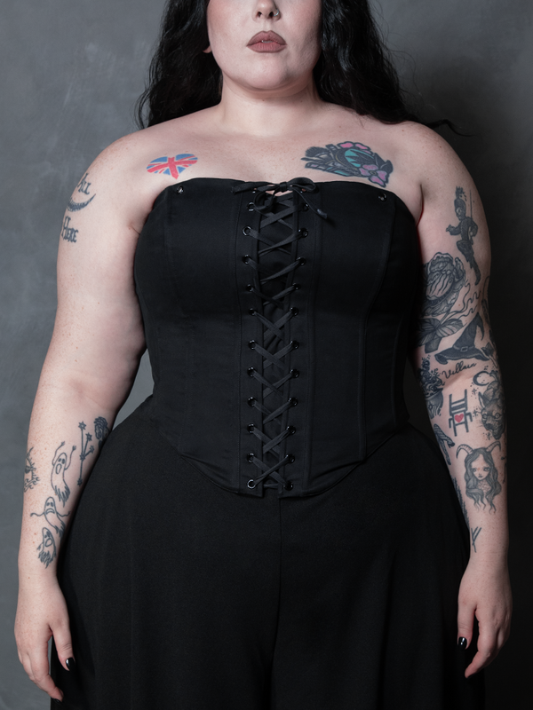 A female model embodies pure gothic glamour, wearing a structured black cotton sateen corset that captures the essence of dark elegance.