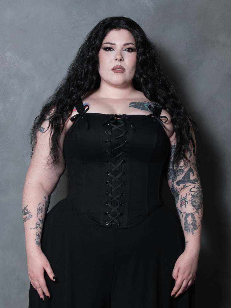 A female model steps into the shadows of dark glamour, wearing a beautifully crafted black sateen gothic corset.
