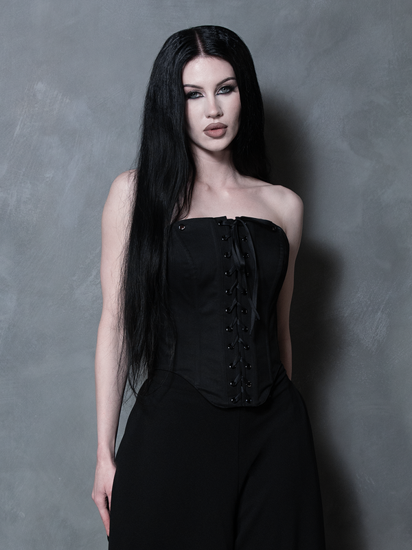 A female model evokes a sense of tragic romance and dark elegance, wearing a luxurious black sateen corset.