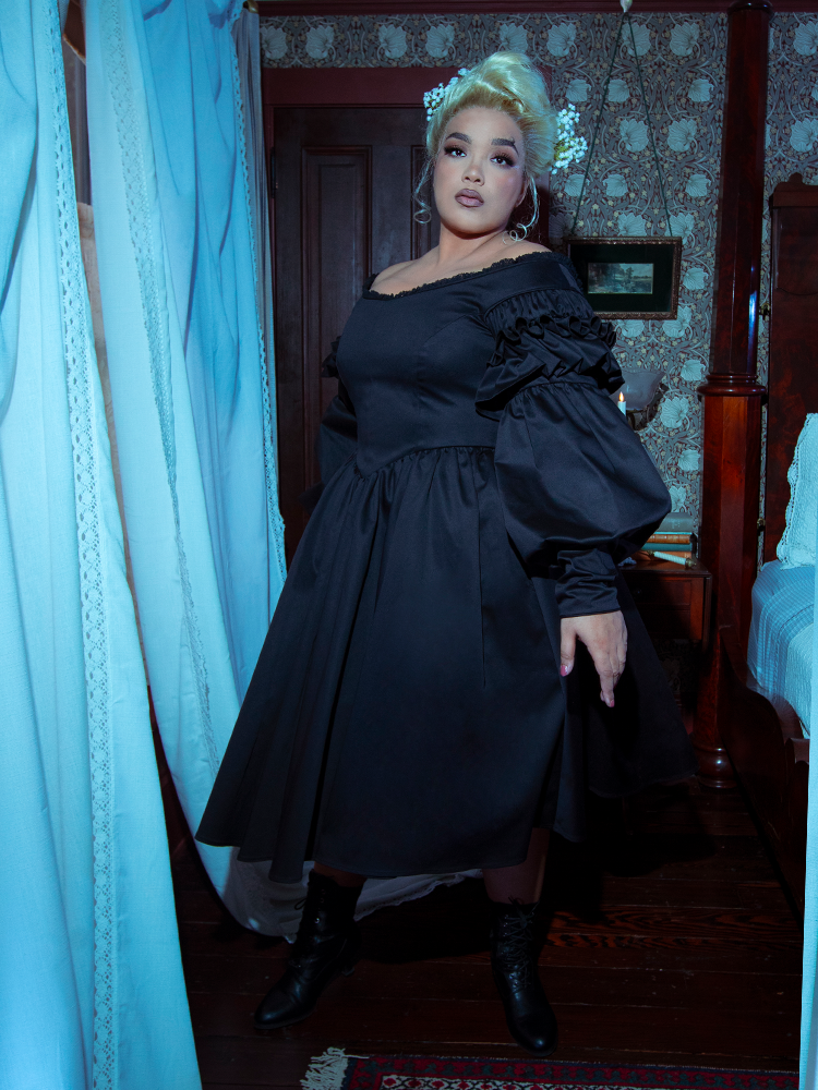 A female model transports us to a bygone era of dark opulence, styled beautifully in the Victorian Goth Ellen Victorian Dress in Black.