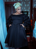 An opulent black Victorian dress with a fitted bodice, delicate lace sleeves, and a floor-length flowing skirt. The high neckline and intricate detailing evoke timeless elegance and gothic allure.