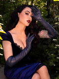 In a secret garden, Micheline Pitt strikes a seductive pose while adorned with the Navy Faux Leather Opera Gloves from the gothic fashion brand, La Femme en Noir.