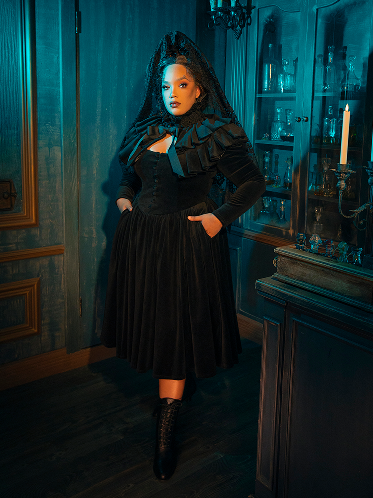  In the folds of this dress, gothic romance is reborn. The black fabric and accompanying capelet are the setting for a tale of love eternal, a romance that whispers through the ages, as timeless as the design itself.