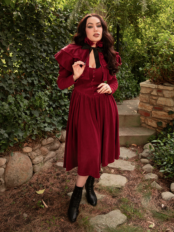 Crimson satin cascades from Micheline Pitt’s shoulders like molten desire—her Haunted Beauty Capelet ignites the night with luxurious rebellion.