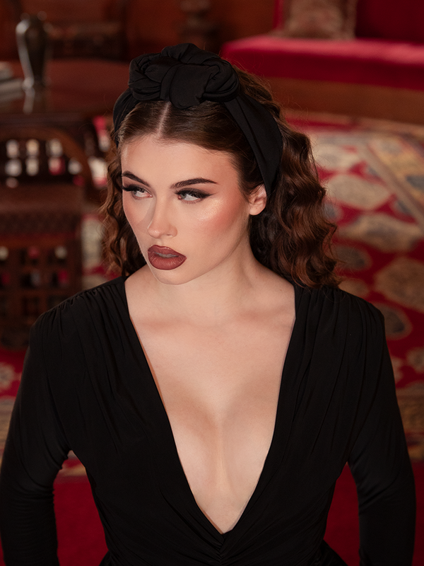A mesmerizing close-up of the Art Deco Knotted Headband in Black, its midnight-hued velvet shimmering with dark elegance, providing the perfect crowning touch for a Victorian Goth aesthetic.