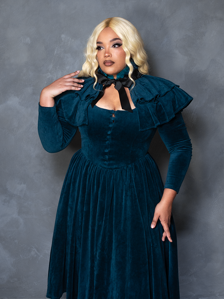Female model wearing the CRIMSON PEAK™ Lady Lucille Victorian Dress with Capelet in Teal, embodying dark elegance and romantic goth fashion.