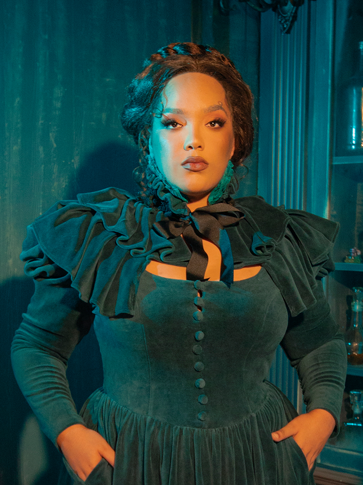 Perfect for those who love vintage gothic fashion, the CRIMSON PEAK™ Lady Lucille Dress in Teal offers a beautifully structured bodice, delicate lace accents, and a capelet that gives the look an extra touch of elegance and drama.