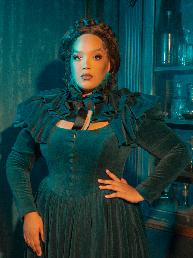 A stunning tribute to Victorian gothic elegance, the CRIMSON PEAK™ Lady Lucille Dress in Teal offers a beautiful silhouette with lace overlays and a regal capelet that adds a touch of vintage mystery.