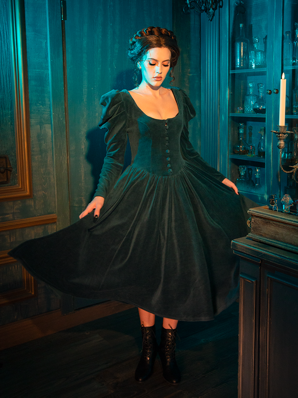 The CRIMSON PEAK™ Lady Lucille Victorian Dress in Teal offers an air of mysterious elegance, featuring delicate lace overlays, a high collar, and a voluminous capelet that adds an aura of romantic gothic beauty.