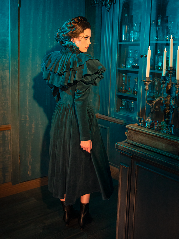 Bring Victorian charm to life with the CRIMSON PEAK™ Lady Lucille Dress in Teal, a stunning creation featuring a high collar, lace detailing, and a dramatic capelet to complete a truly gothic look.