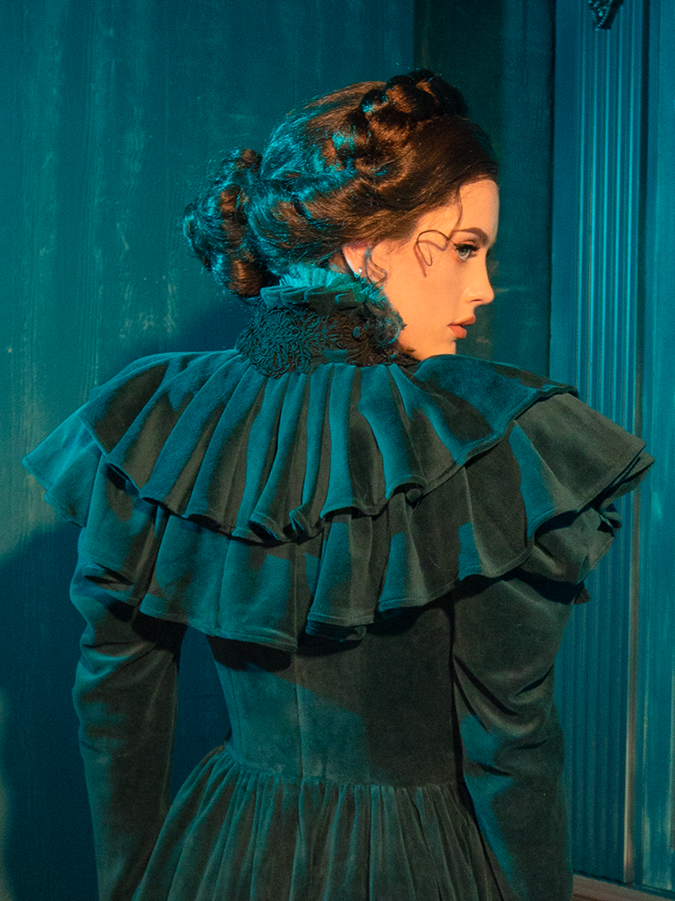 Inspired by Victorian glamour, the CRIMSON PEAK™ Lady Lucille Dress in Teal features a form-fitting bodice, intricate lace overlays, and a stunning capelet to complete your dark, elegant ensemble.