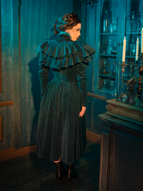 The CRIMSON PEAK™ Lady Lucille Victorian Dress with Capelet in Teal exudes gothic sophistication with its regal design, intricate lace details, and high neckline, making it perfect for those who love vintage-inspired fashion with a dark twist.