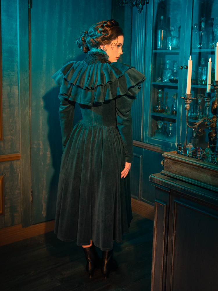 The CRIMSON PEAK™ Lady Lucille Victorian Dress with Capelet in Teal exudes gothic sophistication with its regal design, intricate lace details, and high neckline, making it perfect for those who love vintage-inspired fashion with a dark twist.