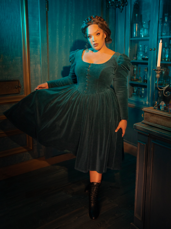 The CRIMSON PEAK™ Lady Lucille Victorian Dress with Capelet in Teal is a show-stopping piece, offering a vintage-inspired silhouette with dramatic lace detailing, a high collar, and an elegant capelet that drapes beautifully.