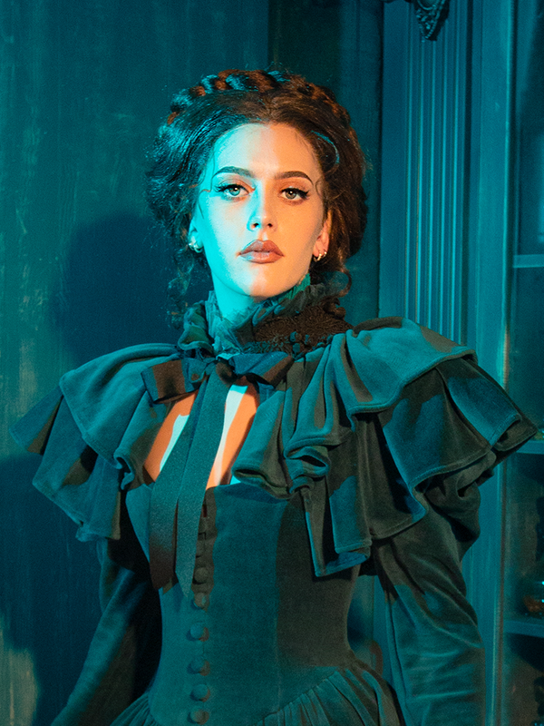 Channel Victorian elegance with the CRIMSON PEAK™ Lady Lucille Dress in Teal, featuring a delicate lace overlay, high-neck design, and flowing capelet for a look that mixes dark romance with timeless sophistication.
