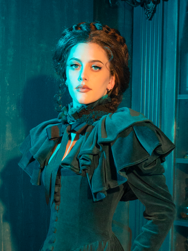 The CRIMSON PEAK™ Lady Lucille Victorian Dress with Capelet in Teal brings the ethereal beauty of the Victorian era to life, complete with lace detailing, a high-neck collar, and a whimsical capelet for added drama.