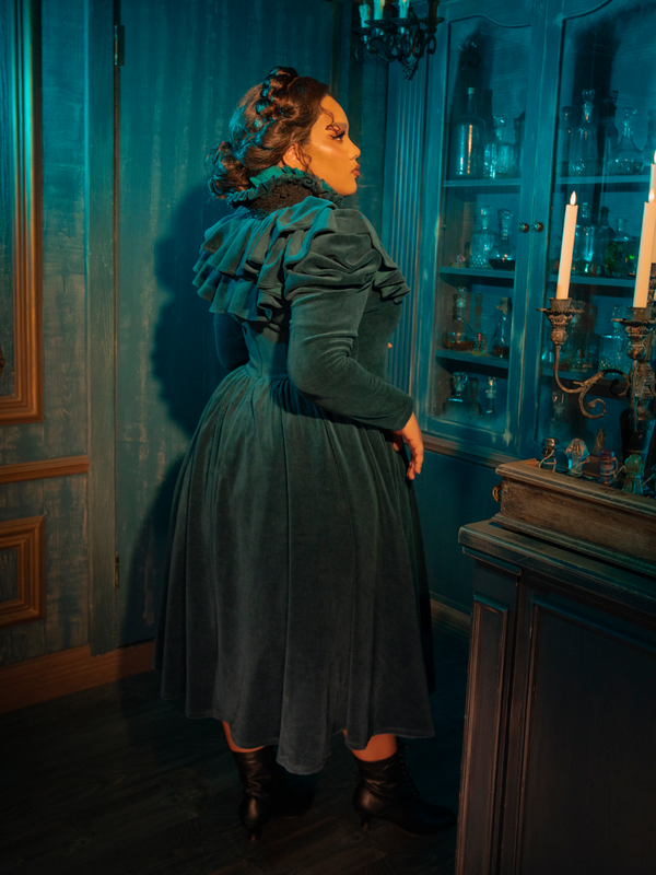 A vision of dark elegance, the CRIMSON PEAK™ Lady Lucille Victorian Dress in Teal features intricate lace overlays, a regal high collar, and a flowing capelet that adds timeless mystery to this beautiful vintage-inspired gown.