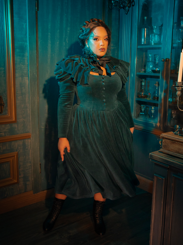 Step into a world of gothic romance with the CRIMSON PEAK™ Lady Lucille Victorian Dress in Teal, featuring a fitted bodice, high-neck design, delicate lace accents, and an ethereal capelet that exudes dark glamour.