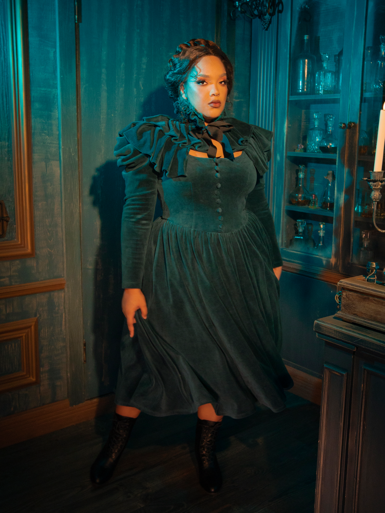 Step into a world of gothic romance with the CRIMSON PEAK™ Lady Lucille Victorian Dress in Teal, featuring a fitted bodice, high-neck design, delicate lace accents, and an ethereal capelet that exudes dark glamour.