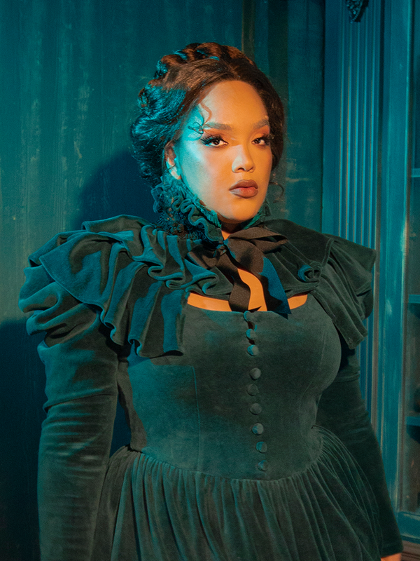 A perfect blend of Victorian romance and gothic allure, the CRIMSON PEAK™ Lady Lucille Dress in Teal features an intricately detailed bodice, delicate lace overlays, and a stunning capelet to complete the look.