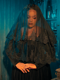 Emanating a sense of pensive contemplation and darkness, a Gothic female model skillfully showcases the Ornate Victorian Lady Mourning Veil from the gothic clothing brand La Femme en Noir, adopting poses that convey a mysterious and introspective allure.