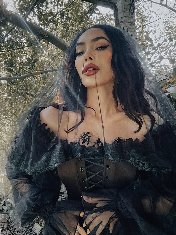 The veil flows down the back like a river of shadows, its embroidered lace trim adding weight and grace to every movement.