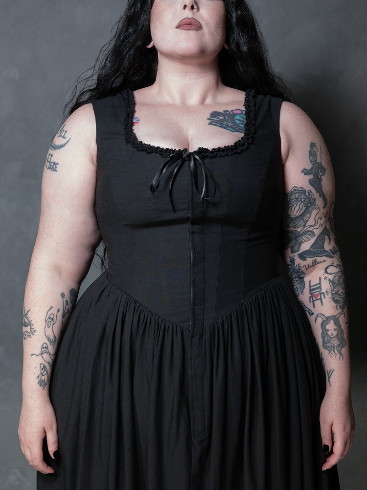 A female model showcases the breathtaking artistry of gothic glamour fashion, wearing the timeless Nightshade Underpinning Dress in Antique Black.
