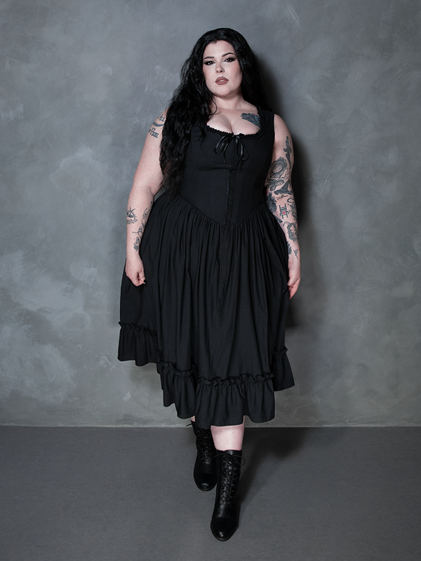 A female model commands attention with an air of sophisticated melancholy, wearing the stunning Nightshade Underpinning Dress in Antique Black.