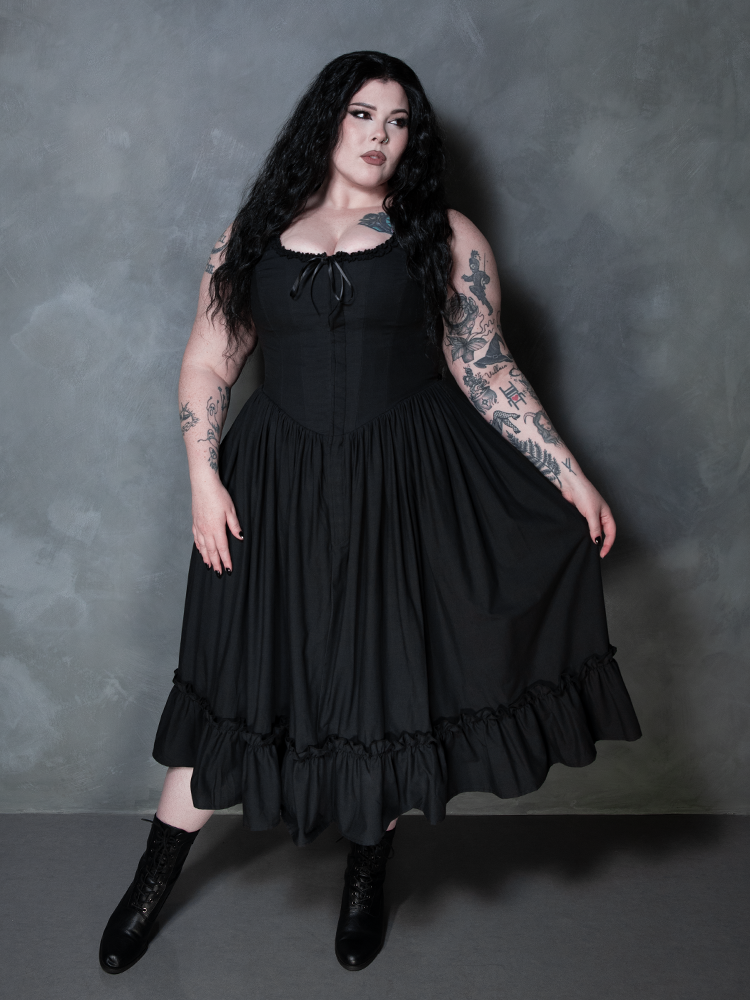 A female model steps from the shadows, a striking silhouette of dark elegance in the Nightshade Underpinning Dress in Antique Black.