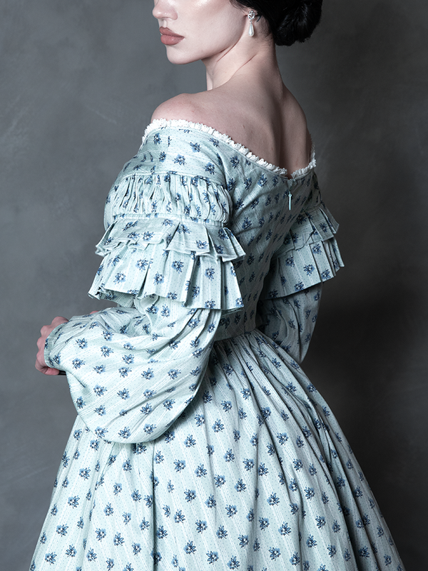 Steeped in romantic melancholy, a model styled in Whimsigoth inspired clothing showcases a sweeping blue botanical dress that captures the timeless spirit of gothic horror.