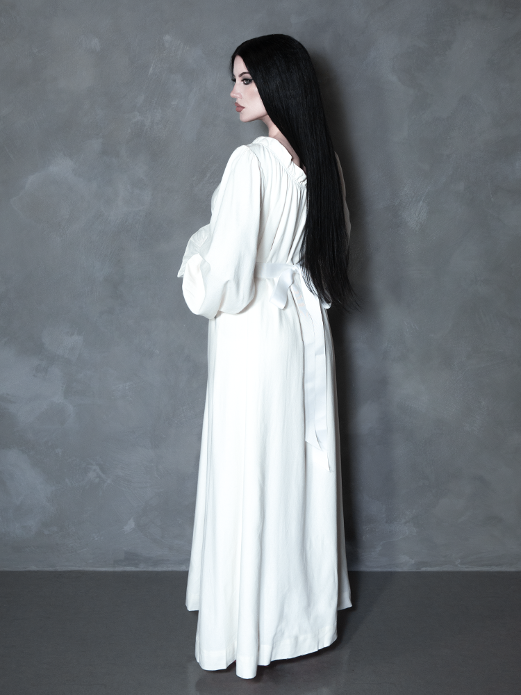 A gothic glamour icon channels the mysterious depth of a haunted manor while draped in a premium, pale ivory dress meant for the ultimate alternative aesthetic.
