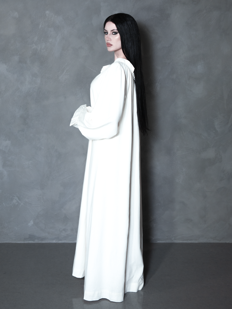 Radiating a sense of tragic romance and cinematic history, a female model wears a flowing piece of dark alternative apparel featuring a haunted, Victorian-inspired pale design.
