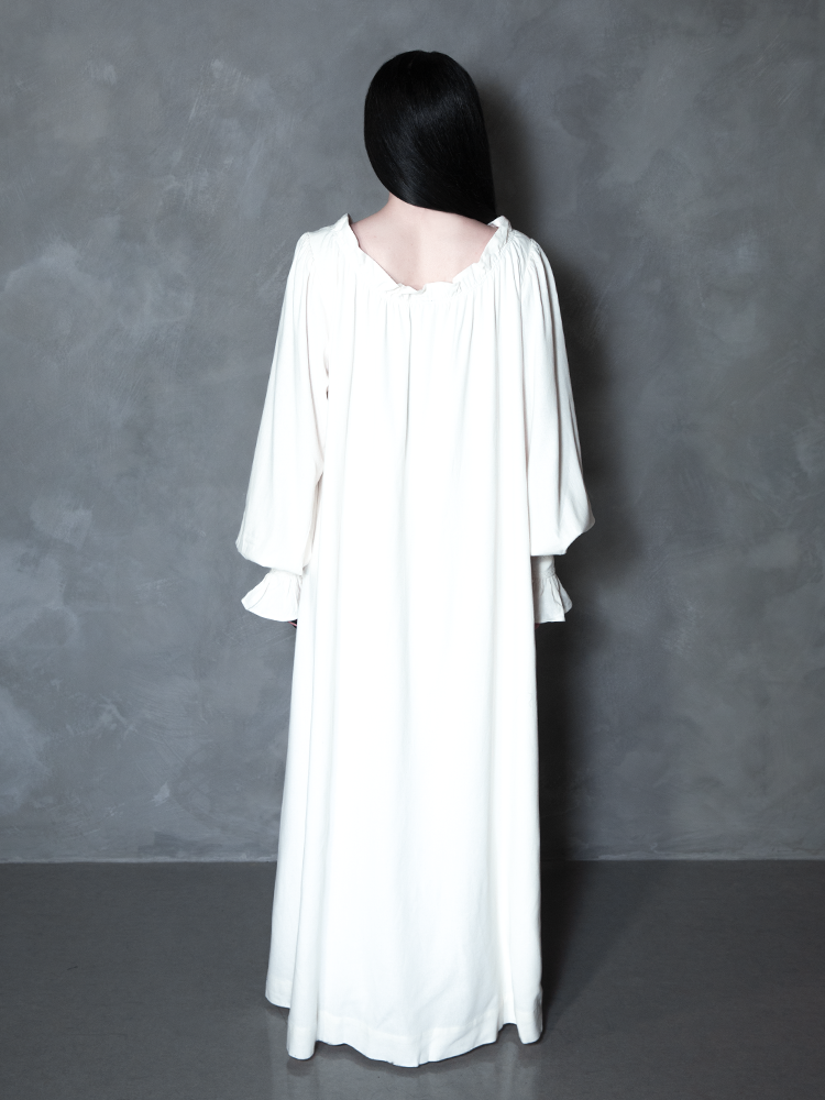 A model effortlessly blends regal comfort with a high-fashion Victorian Goth allure, showcasing a dramatic, ivory nightgown perfect for moonlit strolls.