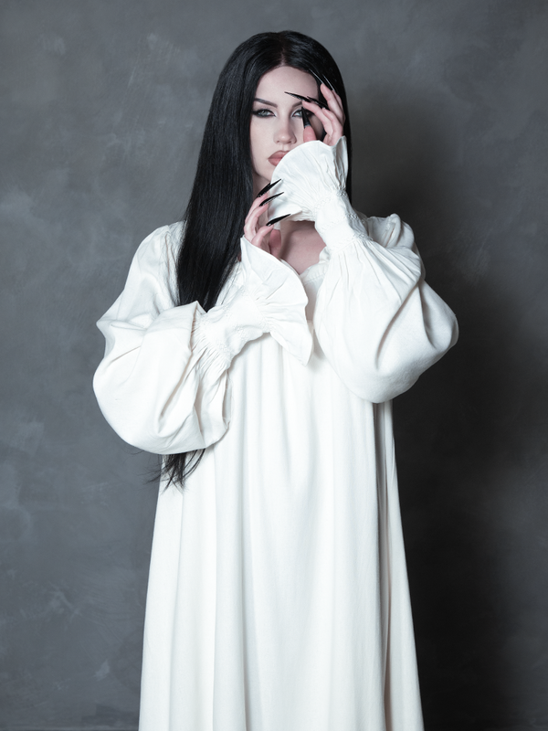 A striking vision of dark elegance, a female model embodies gothic glamour in a beautifully tailored, alabaster-hued sleeping gown steeped in cinematic mystery.