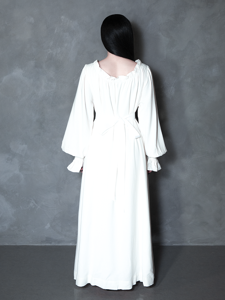 Exuding the essence of dark elegance and Whimsigoth moodiness, a female model layers her look with a hauntingly beautiful, cinematic bone-white gown.
