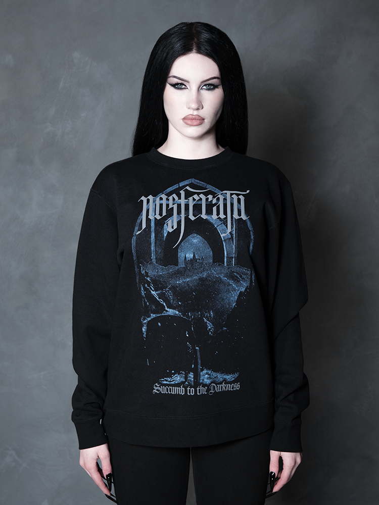 A female model channels high-fashion vampire romance, her darkly enchanting ensemble centered around a premium piece of gothic apparel bearing a sinister fortress design.