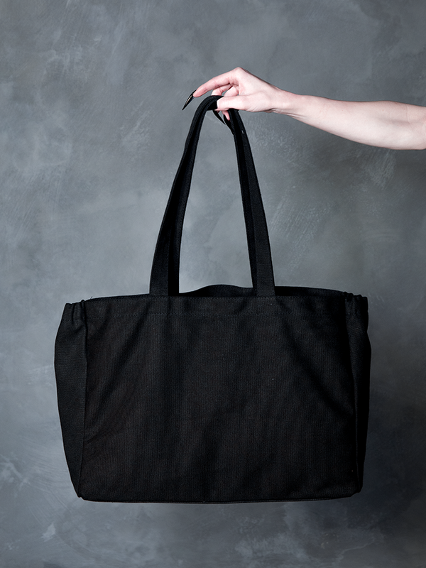 Steeped in romantic melancholy, a model wearing Whimsigoth inspired style clothing coordinates her look with a mysterious, shadow-hued gothic fashion tote bag.