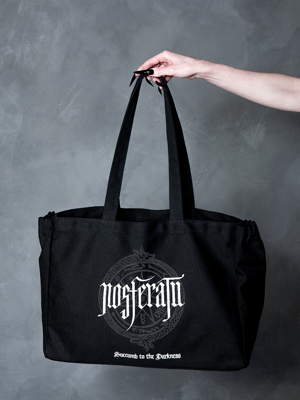 A vision of dark elegance, a female model embodies gothic glamour while showcasing a cinematic, hauntingly beautiful black canvas tote bag bearing a sinister sigil.