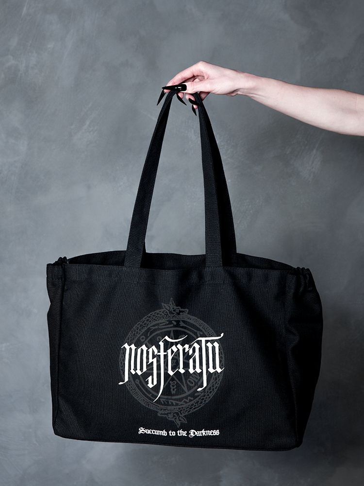 A vision of dark elegance, a female model embodies gothic glamour while showcasing a cinematic, hauntingly beautiful black canvas tote bag bearing a sinister sigil.