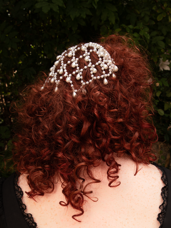 A veil of silver and pearls spills in graceful drops, framing the face in ethereal elegance. Designed for effortless styling; store dry to maintain its luminous finish.