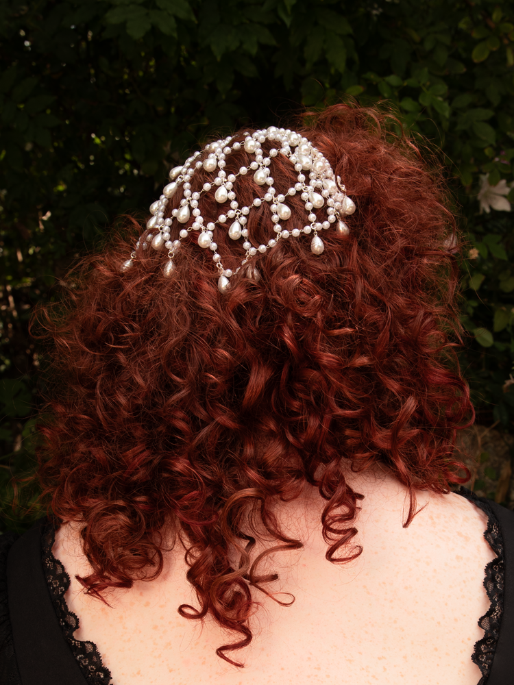 A veil of silver and pearls spills in graceful drops, framing the face in ethereal elegance. Designed for effortless styling; store dry to maintain its luminous finish.