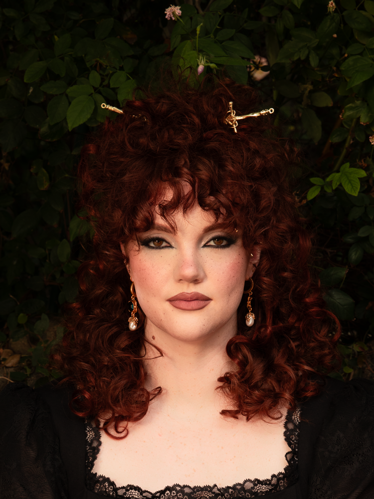 A gleaming sword-shaped hair pin in antique gold, its hilt etched with baroque detail and the blade tapering to a graceful point. Nestled in dark, cascading locks, it evokes the spirit of a gothic warrior queen—delicate yet defiant.