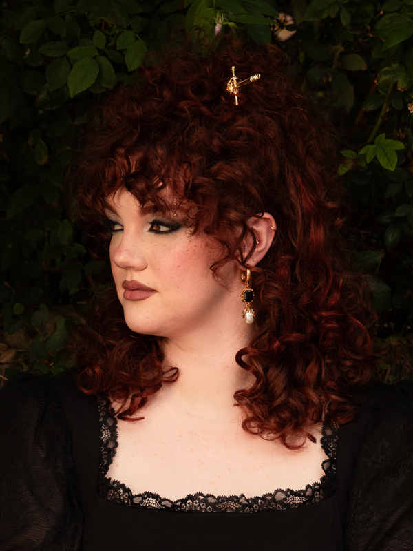 Pinned through a sleek chignon, the golden sword gleams like a relic of ancient nobility. Its ornate design lends an air of regal defiance—equal parts armor and adornment for the modern gothic muse.