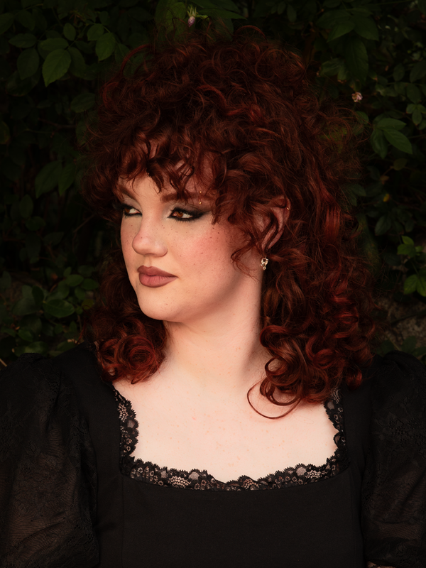 Evoking a timeless Whimsigoth aesthetic, a female model exudes an enchanting, morally gray charm while wearing bold silver skull hoop earrings designed to elevate any gothic style clothing.