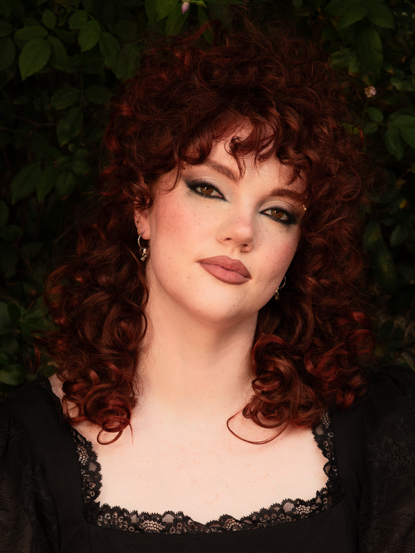 A female model channels pure gothic glamour, her aura steeped in dark elegance as she showcases striking silver skull hoop earrings that effortlessly complement a romantic, modern Victorian Goth look.