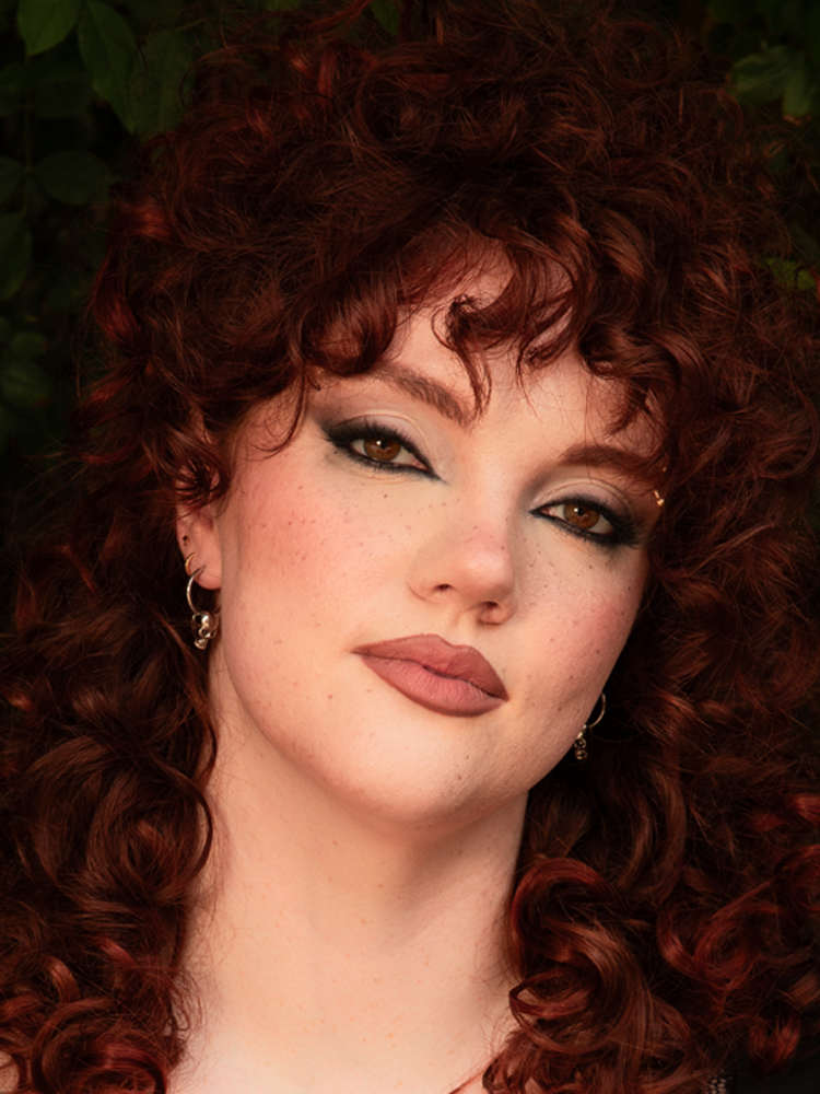A female model embodies the essence of a gothic femme fatale, her look redefined by the rebellious edge of silver skull hoop earrings that infuse dark elegance into her outfit.