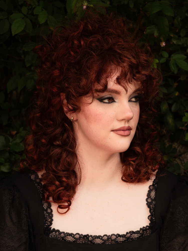 A female model channels a poetic, moody essence, where her commitment to Victorian Goth aesthetics is perfectly highlighted by her silver skull stud earrings.