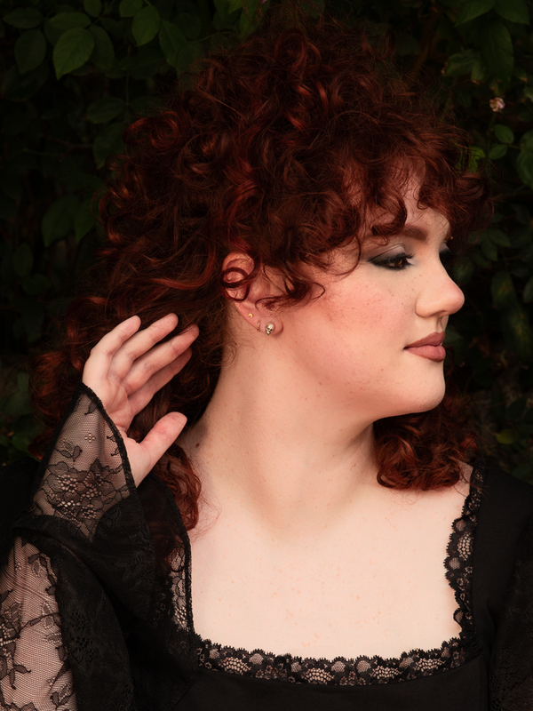 Capturing an aura of quiet dark elegance, a female model subtly enhances her look with silver skull stud earrings that add a touch of gothic glamour to her ensemble.