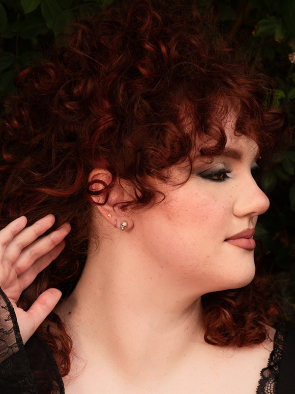 Infused with a classic gothic femme fatale vibe, a female model displays a look of effortless allure adorned with silver skull stud earrings for a hint of dark luxury.